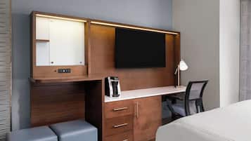 A hotel room with a wooden desk, a flat-screen TV, a coffee maker, a desk lamp, and a bed.