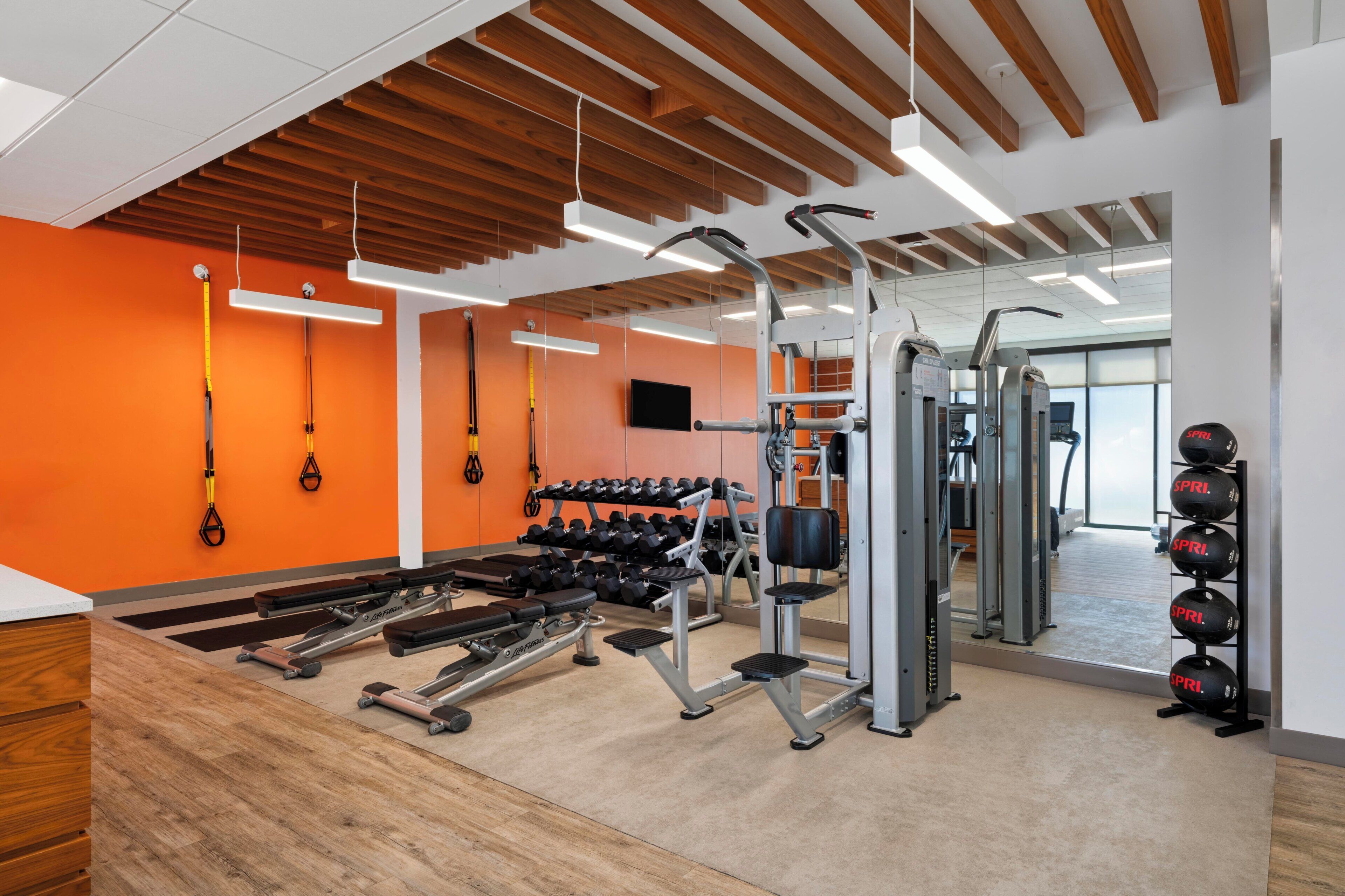 A gym with exercise equipment, a mirrored wall, and orange walls.