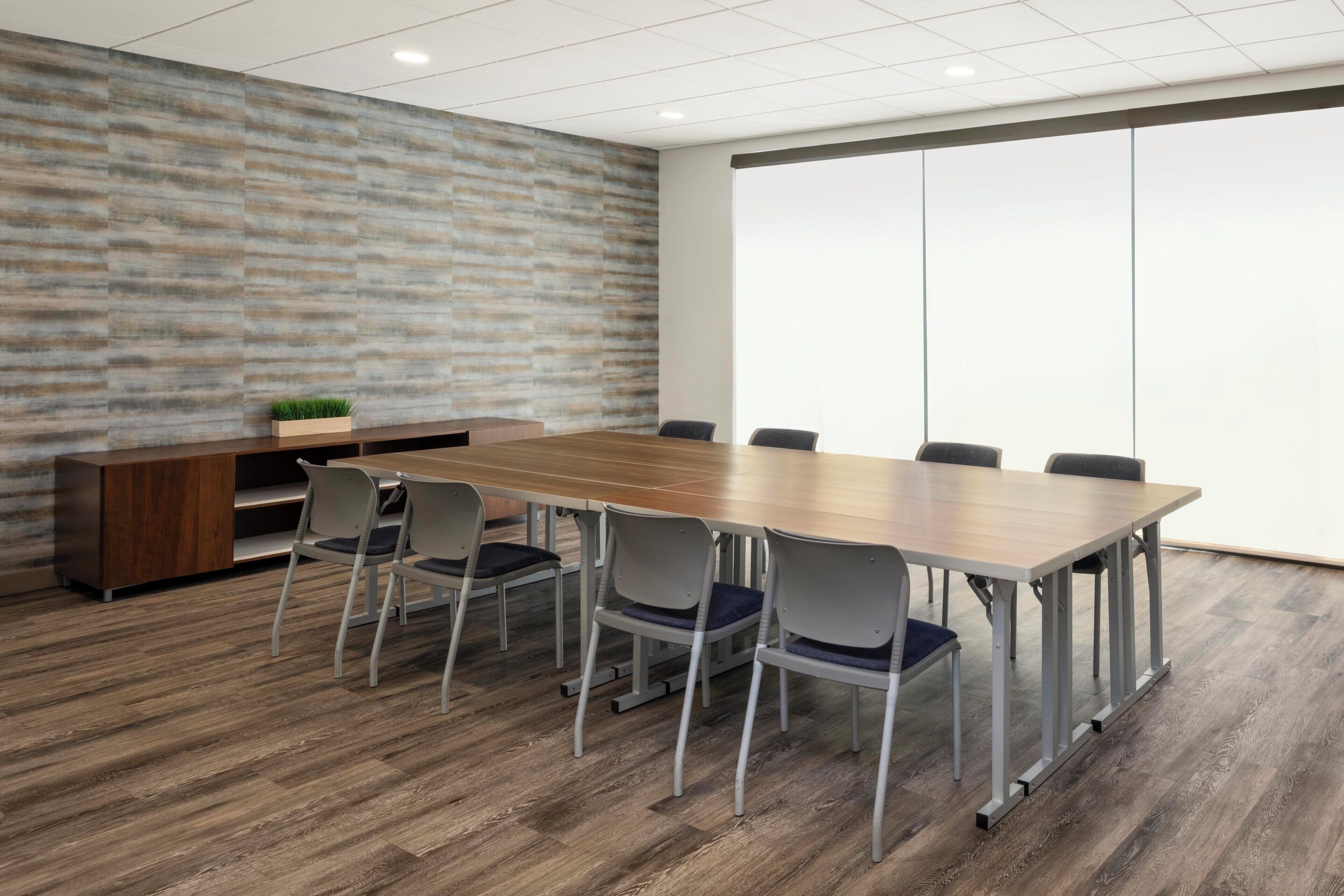 Un salón de conferencias con una larga mesa, seis sillas, un armario de madera y un ventanal grande.