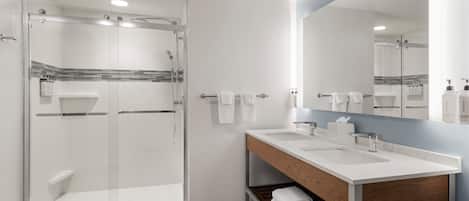 Un baño moderno con ducha envuelta en vidrio, tocador doble y un espejo grande.