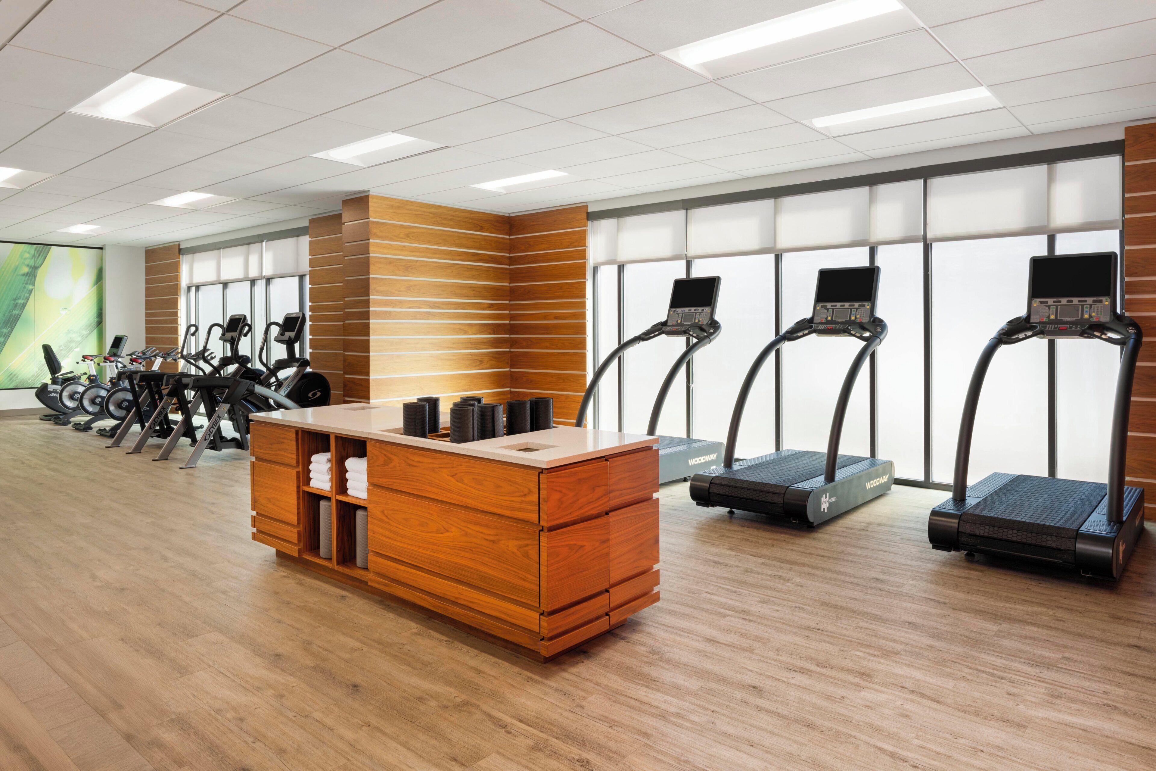 A gym with exercise equipment, a wooden reception desk, and large windows.
