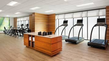 A gym with exercise equipment, a wooden reception desk, and large windows.