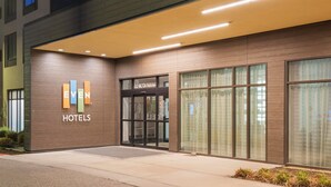 L'entrée d'un hôtel au design moderne, avec une enseigne « EVEN HOTELS » bien visible, une porte d'entrée en verre et une façade bien éclairée.