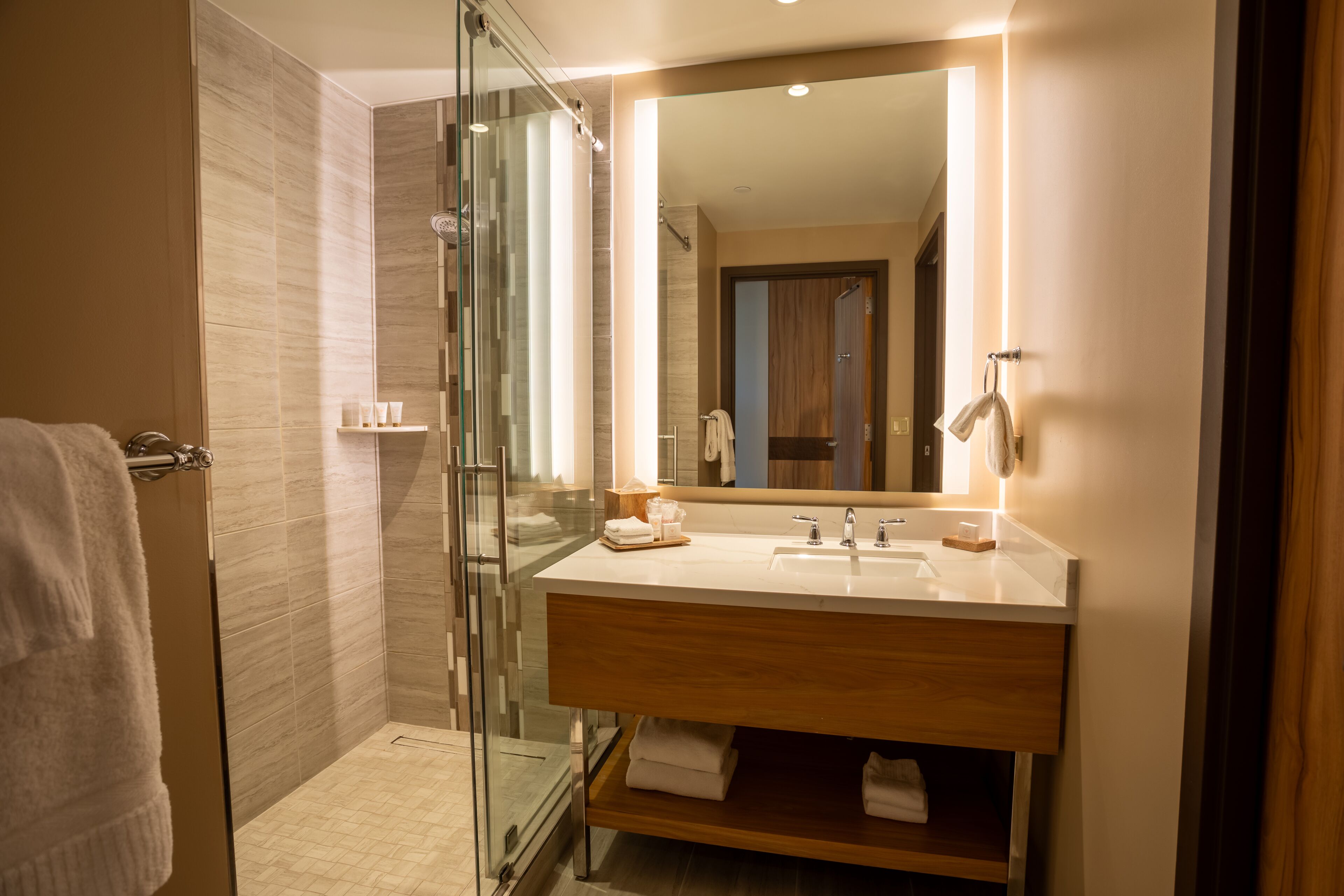 Un baño moderno con cabina de ducha de vidrio, tocador de madera con espejo y un perchero para toallas.