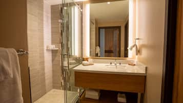 Un baño moderno con cabina de ducha de vidrio, tocador de madera con espejo y un perchero para toallas.