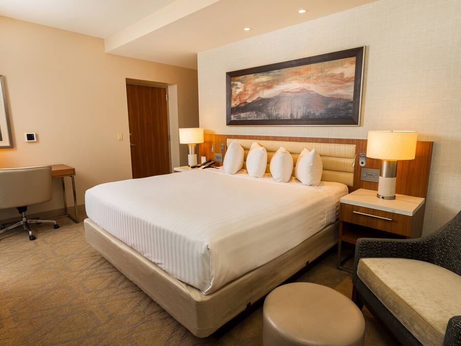 A hotel room with a large bed, two bedside tables with lamps, a desk, a chair, and a painting on the wall.