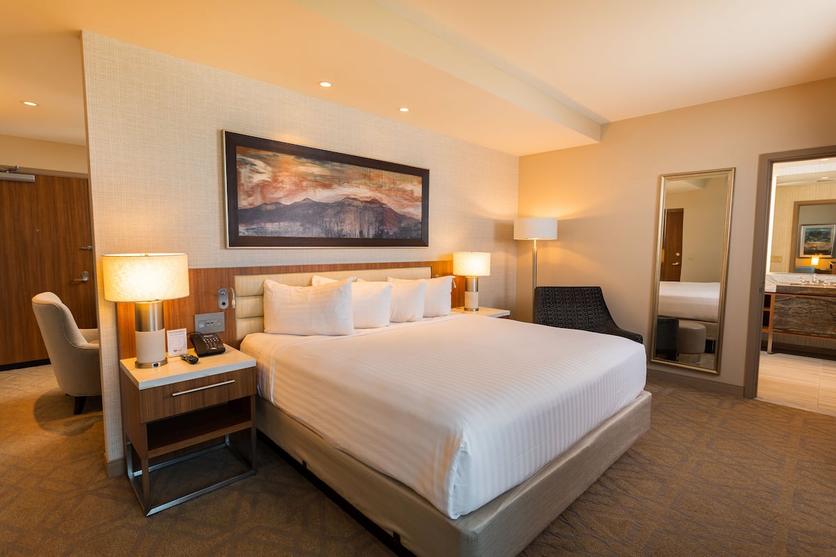 A hotel room with a large bed, bedside lamps, a desk with a lamp, a chair, and a painting on the wall.