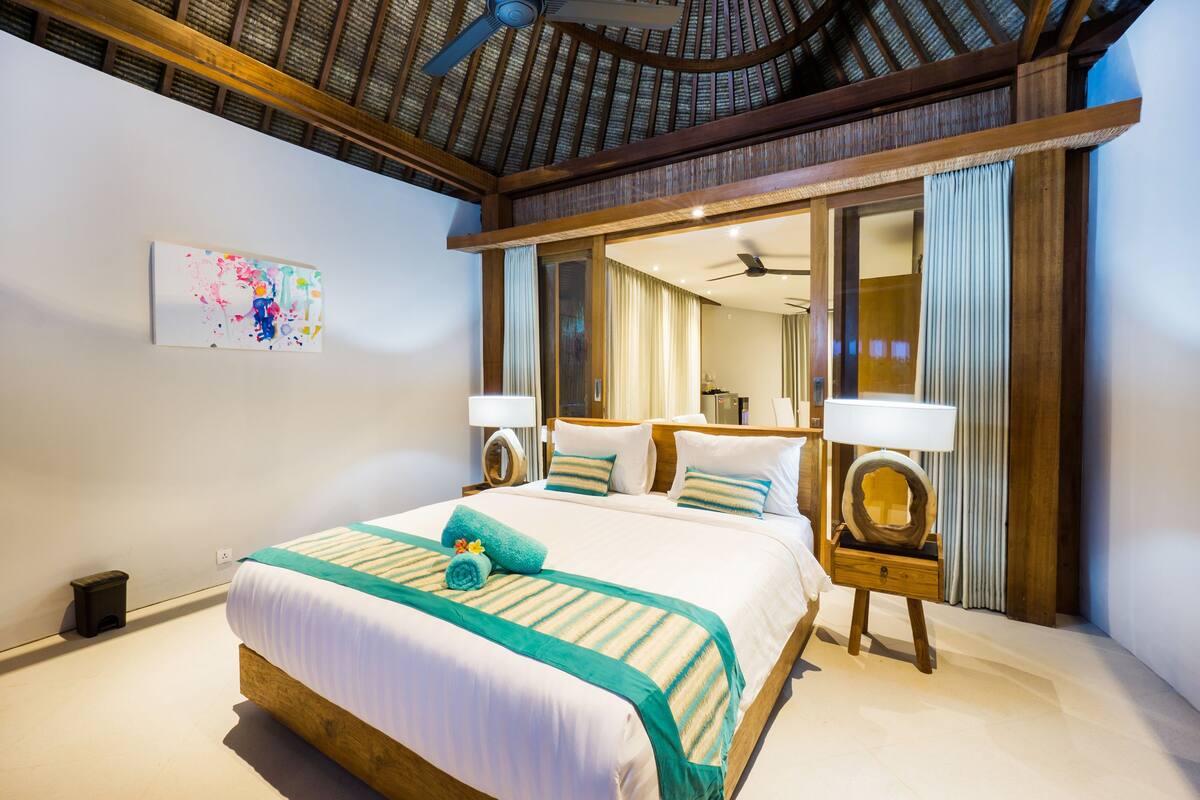 Una habitación de hotel con una cama grande, cabecera de madera y ventilador de techo.