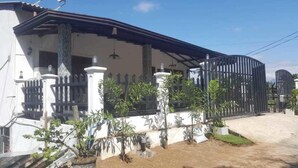 Una casa de dos pisos con un porche cubierto, una reja de metal negro y plantas en macetas en el jardín delantero.