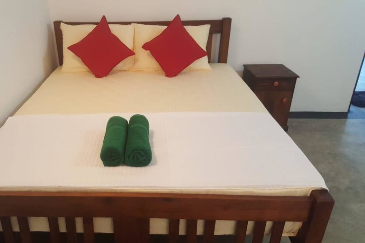 A bed with a white mattress, two red pillows, and two green rolled towels.