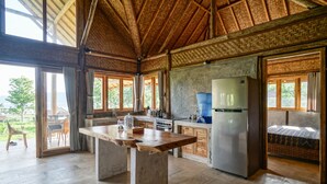 A spacious kitchen with a large island, a refrigerator, and a water dispenser. There are large windows and a view of the outdoors. - Pondok Manoka (Kintamani)