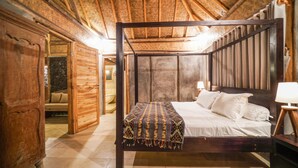A wooden four-poster bed with a patterned throw blanket, a bedside lamp, and a stone wall in the background. - Pondok Manoka (Kintamani)