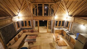 A cozy, rustic interior with a wooden ceiling, a large sofa, a dining table, and a kitchen area. - Pondok Manoka (Kintamani)