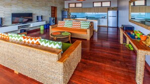 A spacious living area with a large TV, wicker furniture, and a kitchen in the background. - Villa Agung (Lembongan Island)