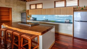 A modern kitchen with wooden countertops, a central island with stools, a built-in refrigerator, and a toaster. - Villa Agung (Lembongan Island)