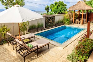 A swimming pool with lounge chairs and a table, surrounded by plants and a decorative wall. - Villa Agung (Lembongan Island)