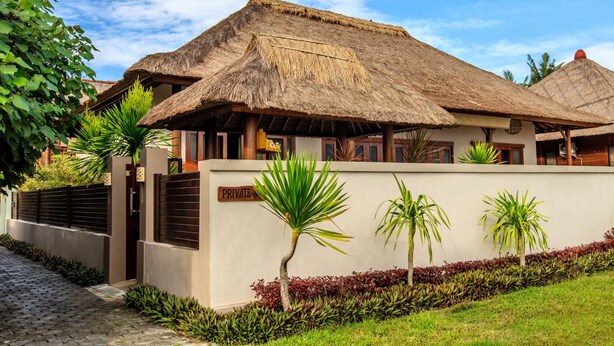 A private villa with a thatched roof, a paved driveway, and a well-maintained garden with tropical plants. - Villa Agung (Lembongan Island)