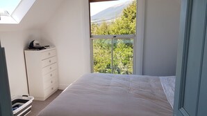 Ein Schlafzimmer mit Dachfenster, einem Bett, einer Kommode und Blick auf eine gebirgige Landschaft.