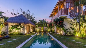 A pool area with a thatched-roof structure, a well-maintained lawn, and a staircase leading to a building with a balcony. - Eco Chic 5BDR Oberoi/ Central Seminyak/beach (Seminyak)