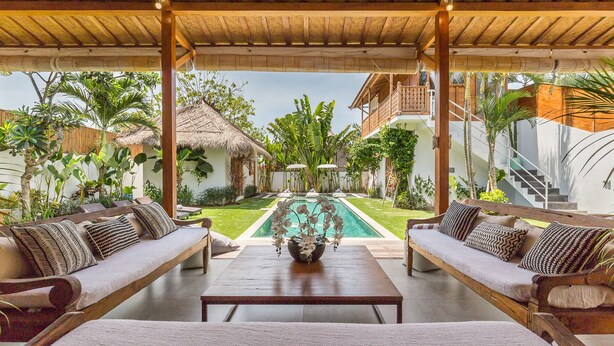 A covered outdoor seating area with two sofas and a table, overlooking a swimming pool and lush garden. - Eco Chic 5BDR Oberoi/ Central Seminyak/beach (Seminyak)