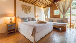 A bedroom with a wooden ceiling, a bed with white bedding, a nightstand with a lamp, a sofa with patterned cushions, and a window with curtains. - Eco Chic 5BDR Oberoi/ Central Seminyak/beach (Seminyak)