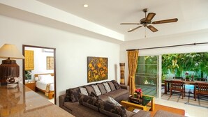 A modern living room with a sofa, coffee table, and a ceiling fan. There is a dining area with a table and chairs visible through a glass door. - Romanee2 Convenient for life private pool Villa (Tambon Rawai)