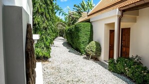 A pathway leading to a building with a tiled roof, surrounded by greenery and a clear blue sky. - Romanee2 Convenient for life private pool Villa (Tambon Rawai)