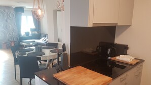 A modern kitchen with a black countertop, wooden cutting board, and white cabinets. There is a dining area with a round table and chairs. - New:Lovely 2.5 Room , Dish Washer, Wifi, Fully Equiped, own washer/dryer (Zürich)