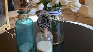 Une cuisine dotée de meubles en bois, d’un réfrigérateur en acier inoxydable et d’un coin repas avec une table agrémentée de bouteilles décoratives et d’un vase de fleurs blanches.