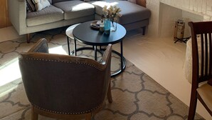 L’intérieur chaleureux d’un chalet avec un plafond en bois, un canapé gris agrémenté de coussins décoratifs, une table basse ronde et une cheminée avec un mur d’accent en pierre.