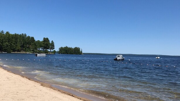 Une plage avec une eau d’un bleu limpide, un bateau et, au loin, une île couverte de forêts.