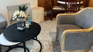 Une pièce chaleureuse aux murs en bois, avec une cheminée, une table ronde entourée de chaises et un téléviseur à écran plat fixé au mur.