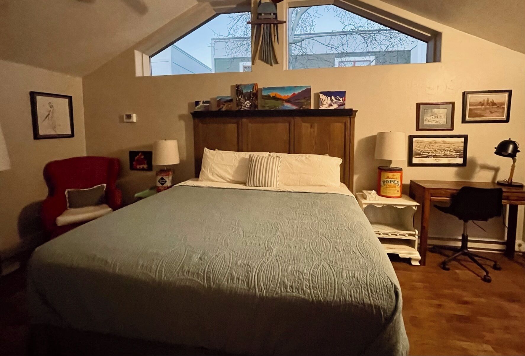 A bedroom with a large bed, a red chair, a desk, and a window with a view of buildings.