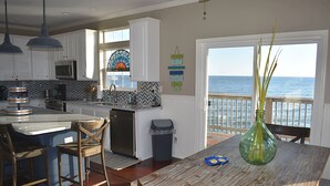A kitchen with a view of the ocean, white cabinets, a wooden dining table, and a green vase. - Key West-style Beach house with Gulf views from nearly every room - Island Time (Dauphin Island)