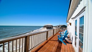 A wooden deck with a railing overlooking a beach, a small structure on stilts, and a building with large windows. - Key West-style Beach house with Gulf views from nearly every room - Island Time (Dauphin Island)