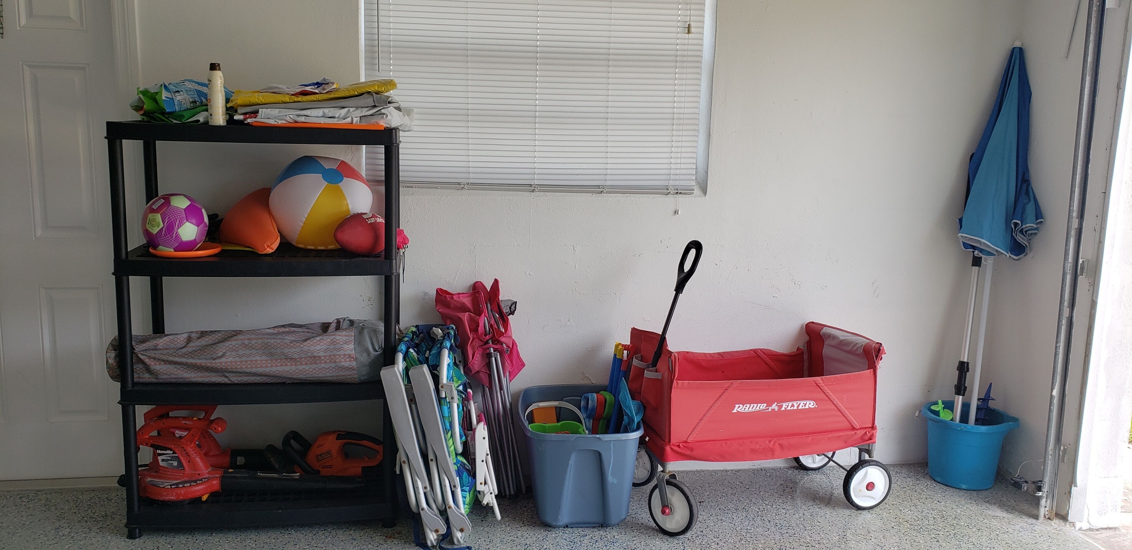 A room with a black shelf holding various items, a red wagon, and a blue bucket.