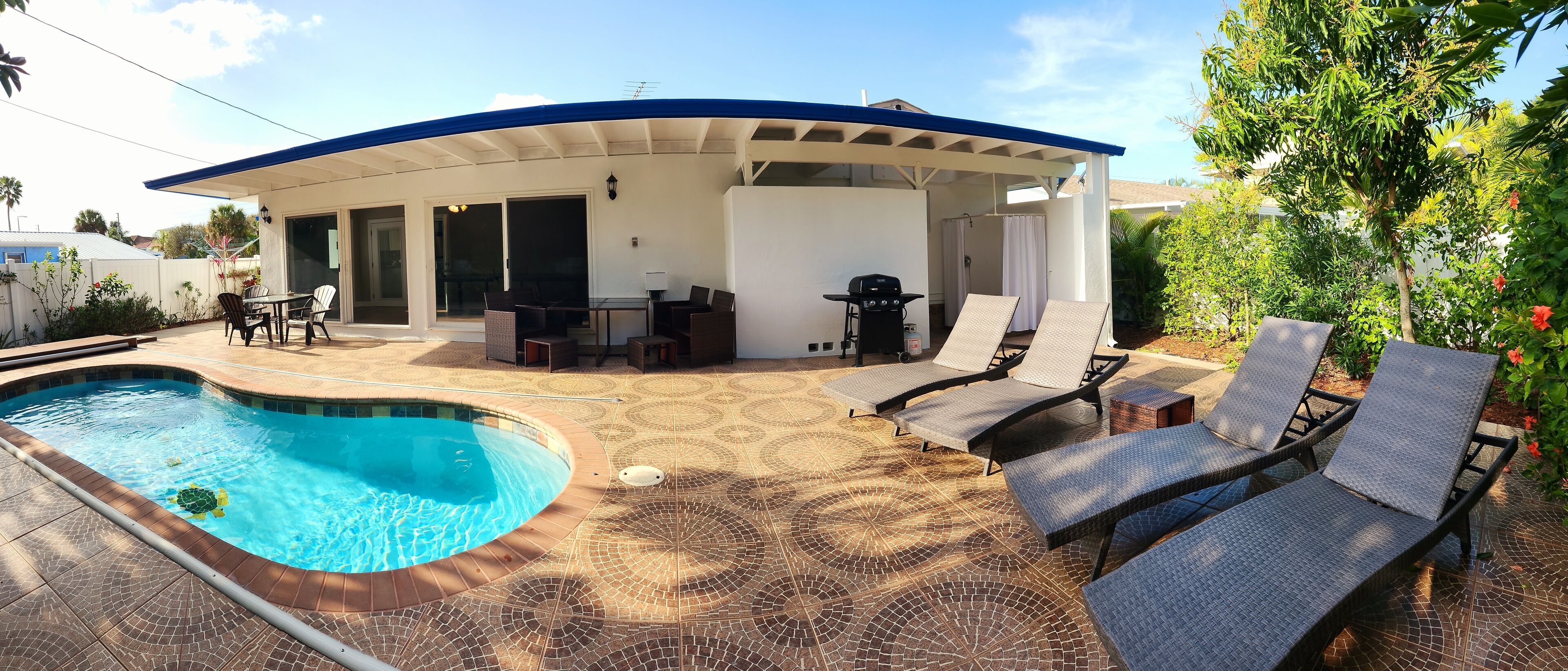 A covered outdoor area with a pool, lounge chairs, and a barbecue grill.