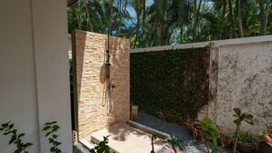 A modern outdoor shower area with stone walls and a tiled floor, surrounded by lush greenery and palm trees.
