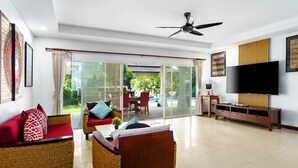 A modern living room with wicker furniture, a flat-screen TV, and a sliding glass door leading to a patio with outdoor seating.