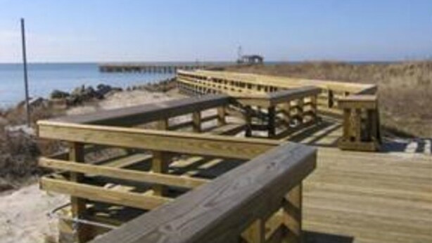 Een houten looppad dat naar een strand leidt, met een pier op de achtergrond.