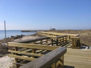 Een houten looppad dat naar een strand leidt, met een pier op de achtergrond.