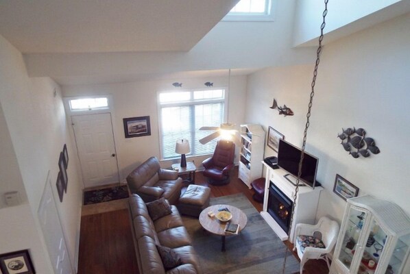 A living room with a sofa, armchair, coffee table, fireplace, TV, and a bookshelf. - Park Place - Comfy Condo Close to Beach (Cape Charles)