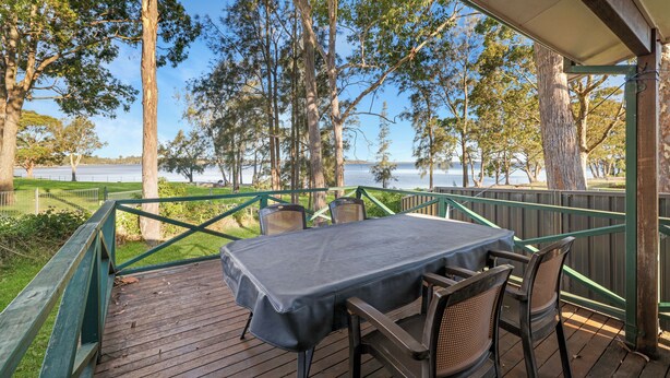 A covered outdoor deck with a table and chairs, overlooking a body of water and trees. - Absolute Waterfront - large deck, level access to water, plenty wildlife (St Georges Basin)