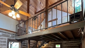 Une cabane en rondins avec une chambre à coucher à l’étage, un coin repas et un escalier.