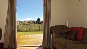 A room with two sofas facing a sliding glass door leading to a balcony with a mountain view. - Piwari Villa  - Summer Hike & Bike, Winter Snow & Spa  (Rangataua)