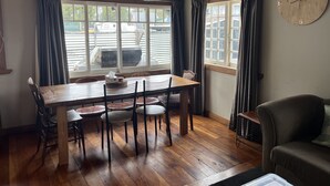 A dining area with a wooden table and chairs, a clock on the wall, and large windows with curtains. - Piwari Villa  - Summer Hike & Bike, Winter Snow & Spa  (Rangataua)