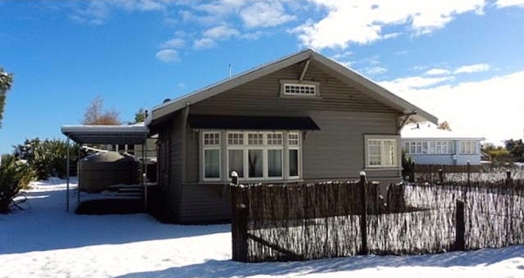 A single-story house with a sloped roof, a covered porch, and a fenced yard.