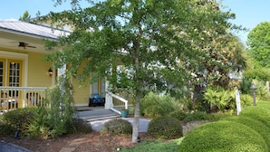 A yellow house with a porch, surrounded by well-maintained landscaping and a variety of plants.