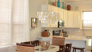 A dining area with a glass-top table, wooden chairs, and a hanging light fixture.