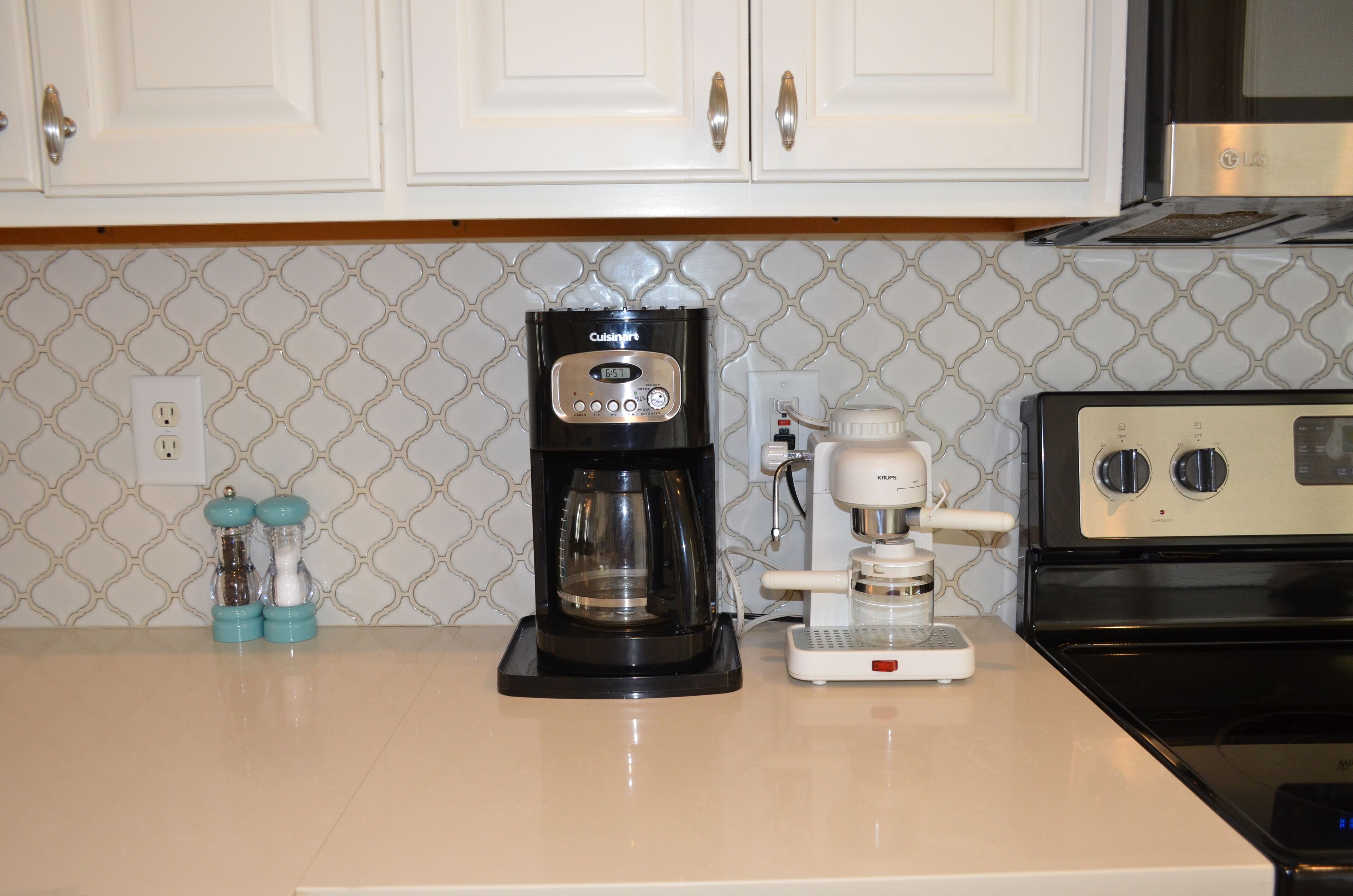 Una cocina con gabinetes blancos, cafetera, tostadora y estufa.